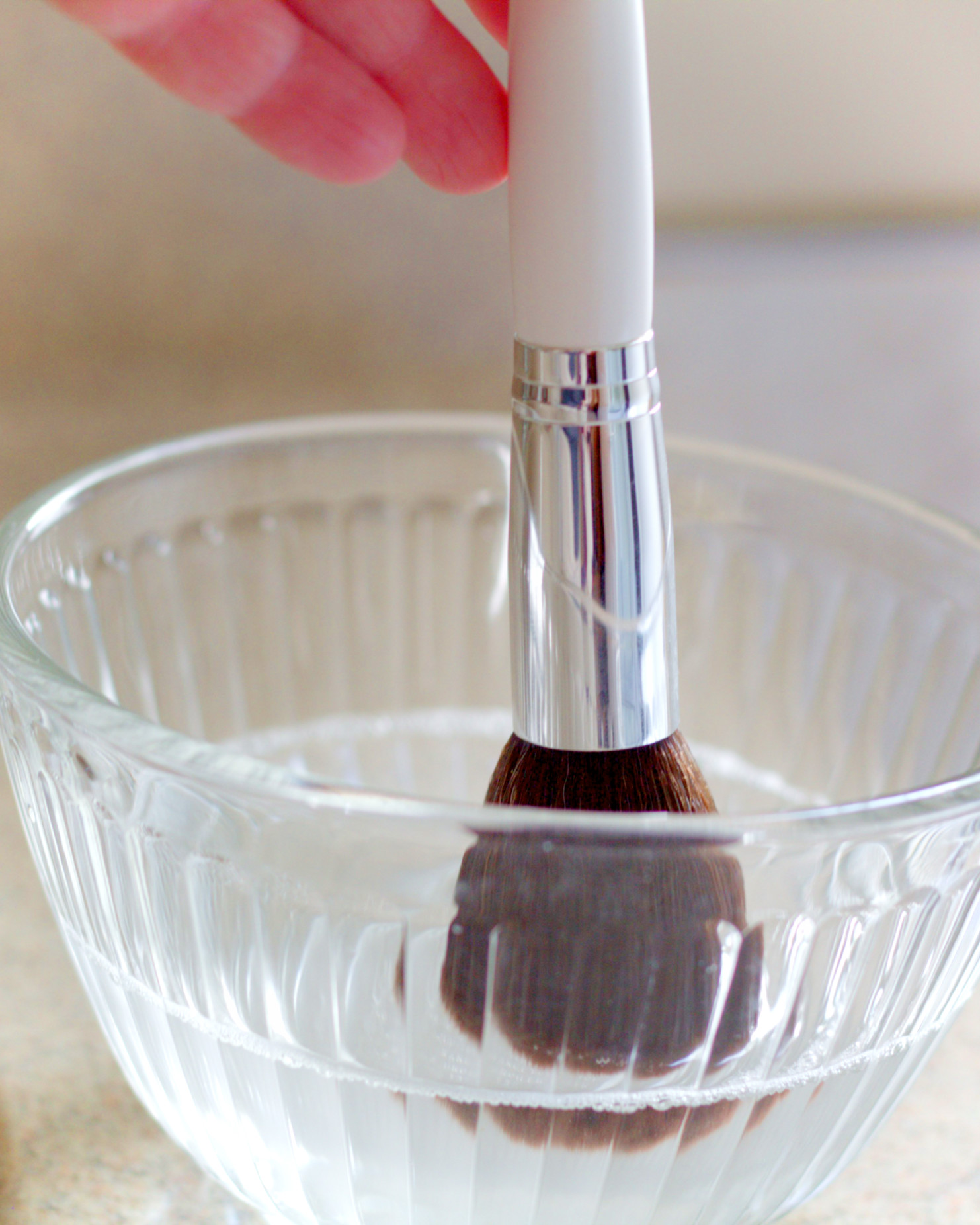 Cleaning A Makeup Brush In A Bowl Of Water Mixed With Cleanser